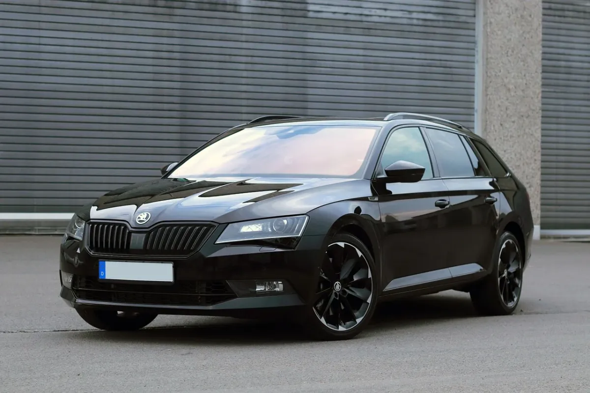 Srebrna Skoda Superb zaparkowana przed nowoczesnym biurowcem w świetle zachodzącego słońca.
