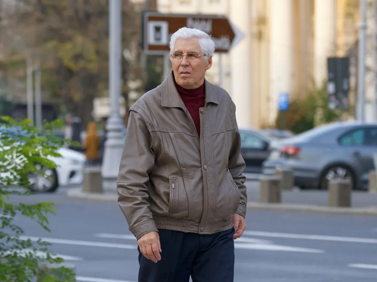 Starszy mężczyzna w kurtce prezentujący ofertę używanych samochodów w komisie.