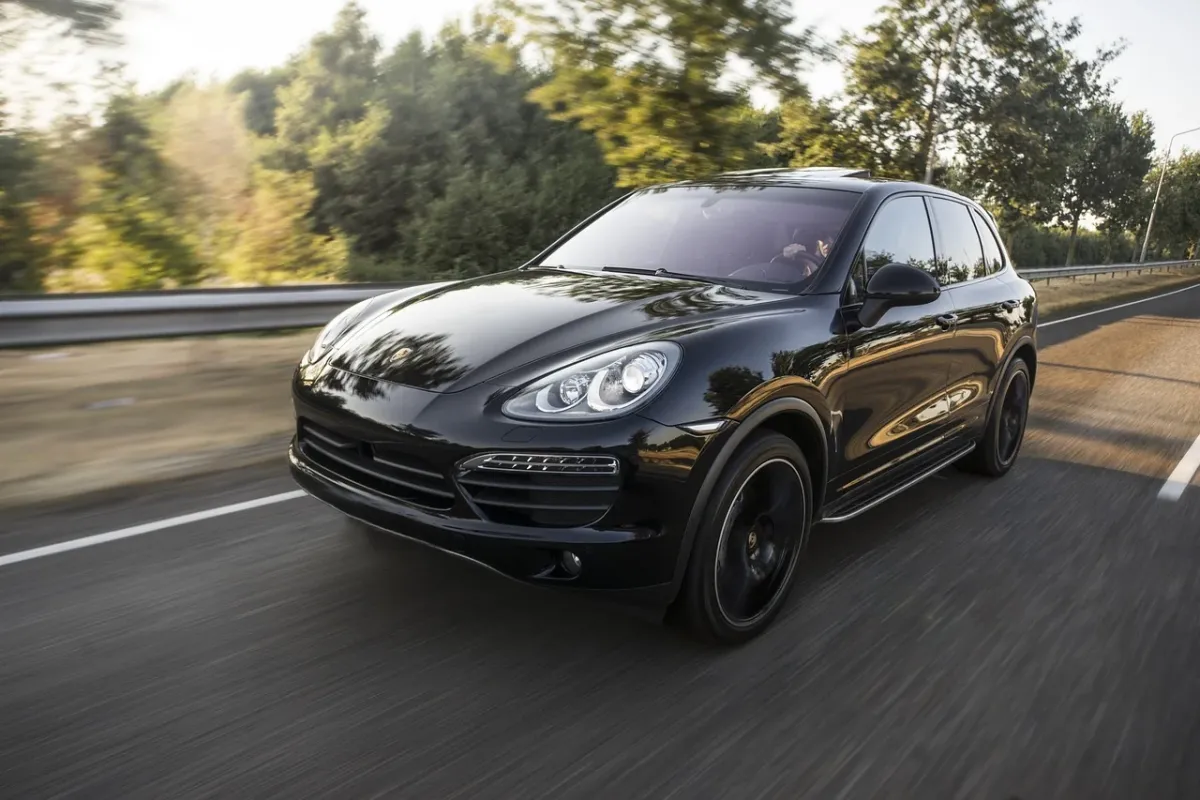 Srebrny Porsche Cayenne i szary Cayenne Coupe zaparkowane obok siebie na tle górskiej drogi w świetle zachodzącego słońca.