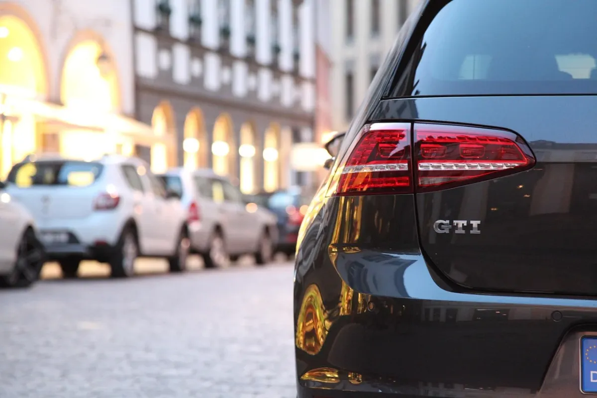Zbliżenie na emblemat GTI na czarnym grillu Golfa 7, z rozmytym torem wyścigowym w tle podczas zachodu słońca.